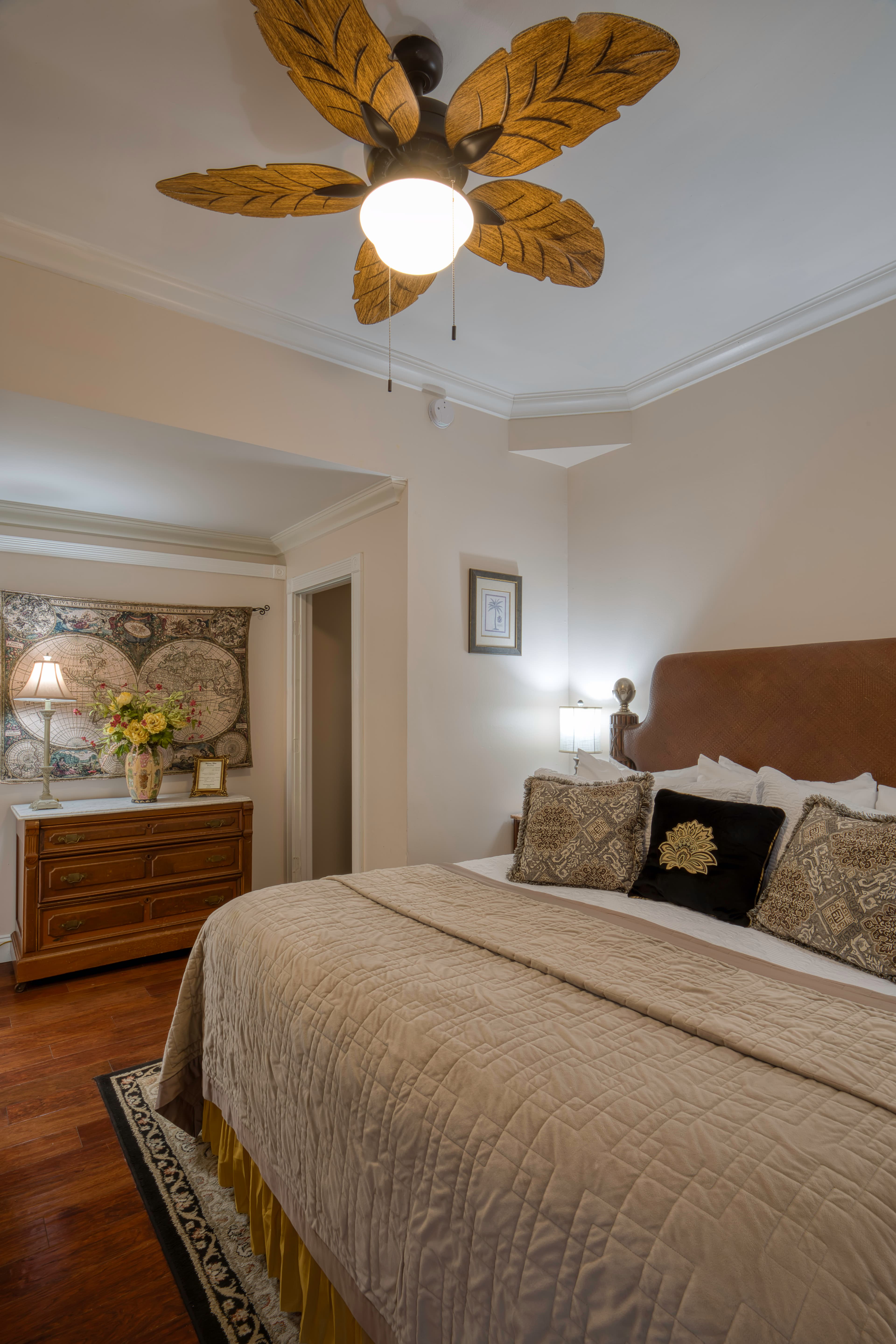 Bedroom with inviting king bed in neutral tones, ceiling fan with leaf-shaped blades, and wooden dresser