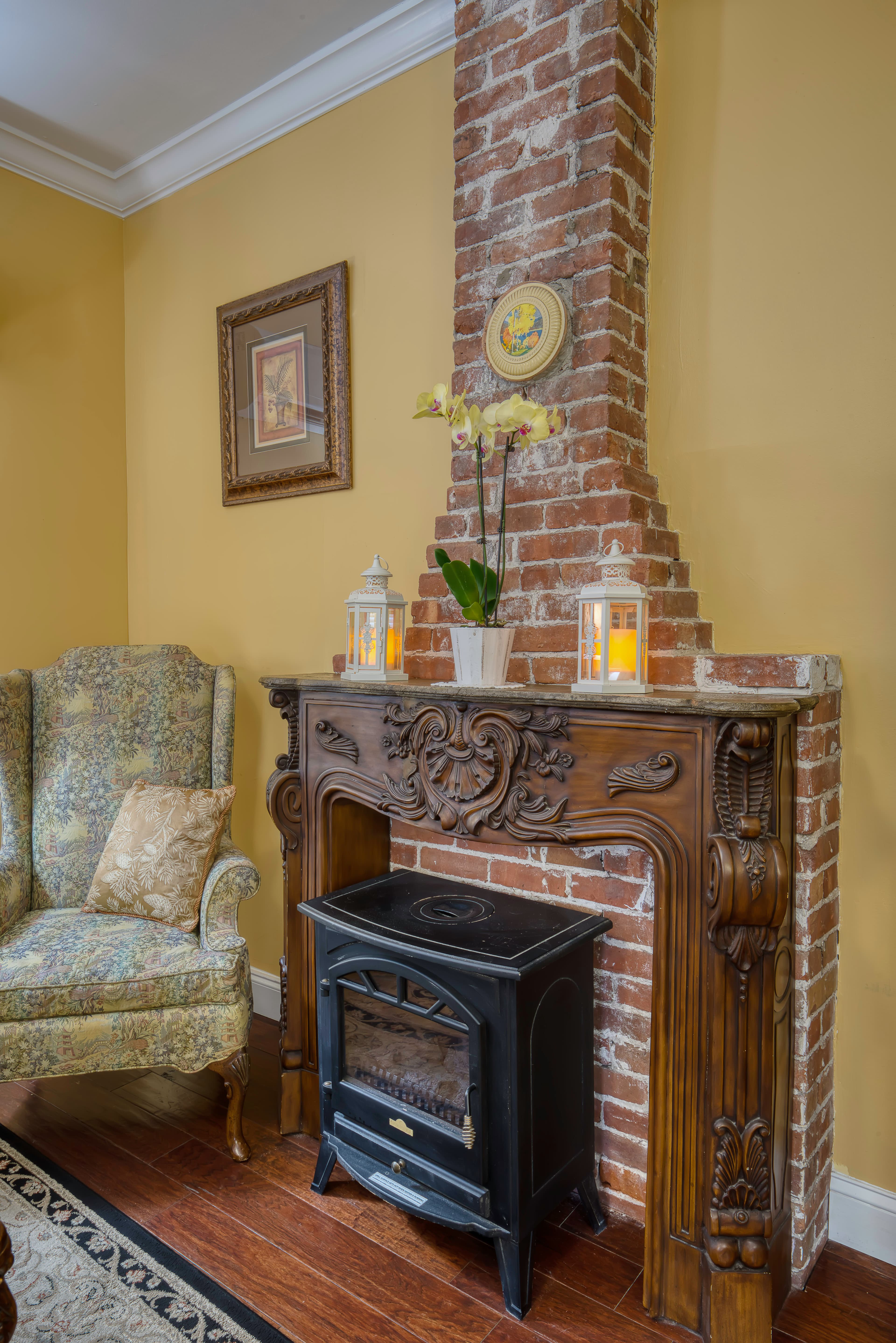 Sitting area with cozy high-back armchair and electric fireplace with brick chimney and ornate wood mantle