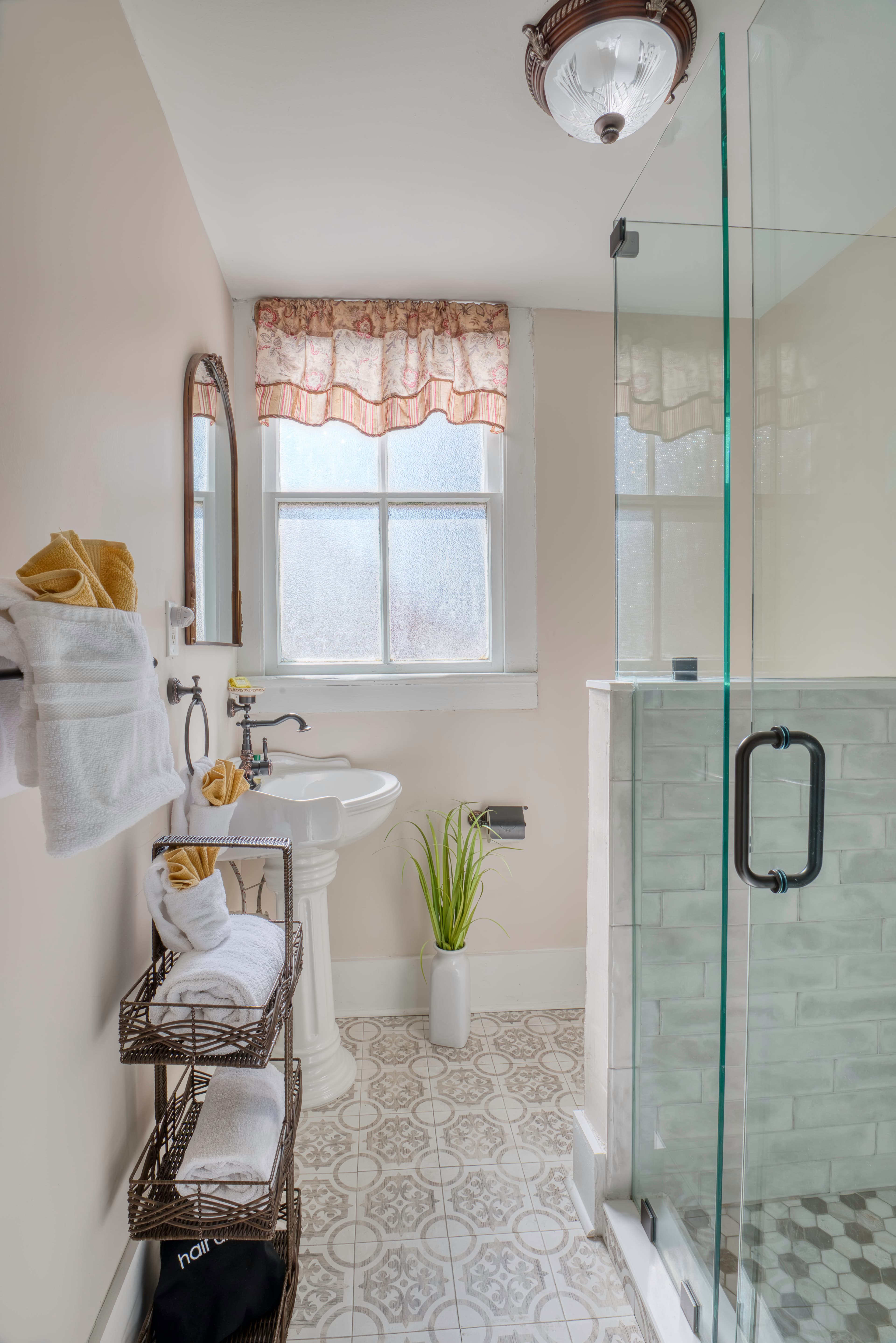 Light and airy bathroom with glass-enclosed walk-in shower, white pedestal sink, and plush white towels
