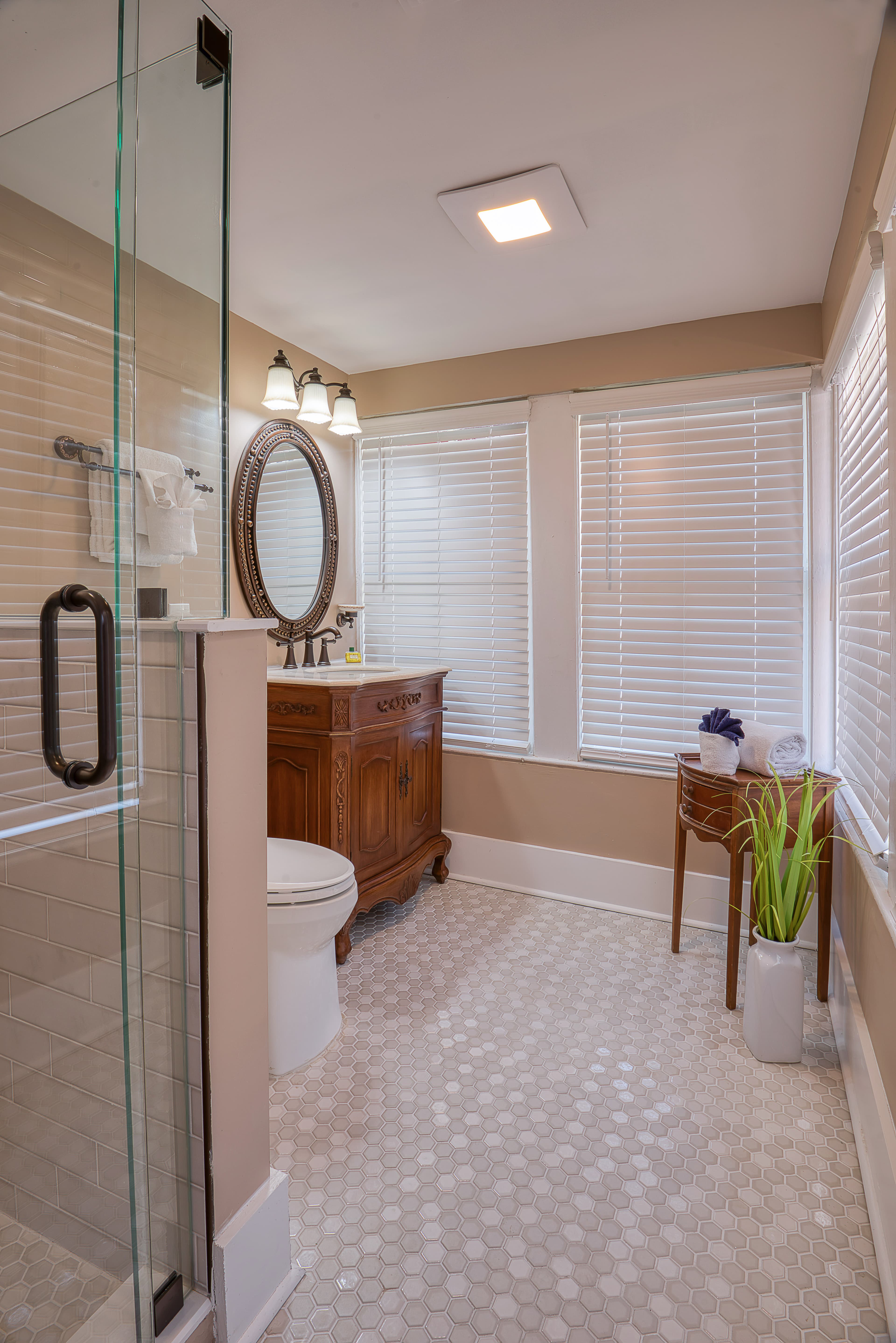 Bathroom decorated in soothing neutral shades with glass-enclosed shower, toilet, wooden vanity with sink and mirror