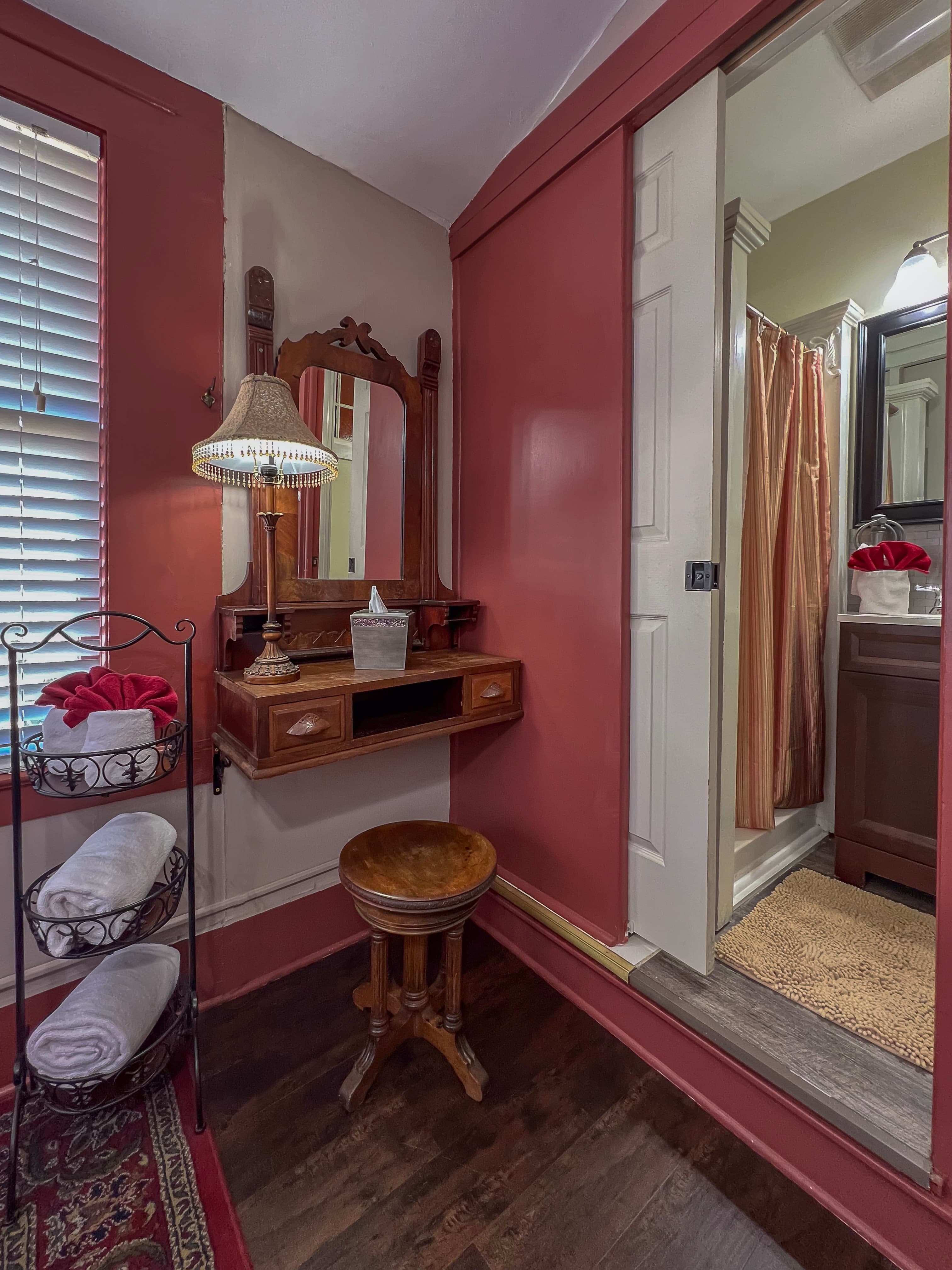 Wooden vanity & stool in corner of bedroom and view through doorway into bathroom