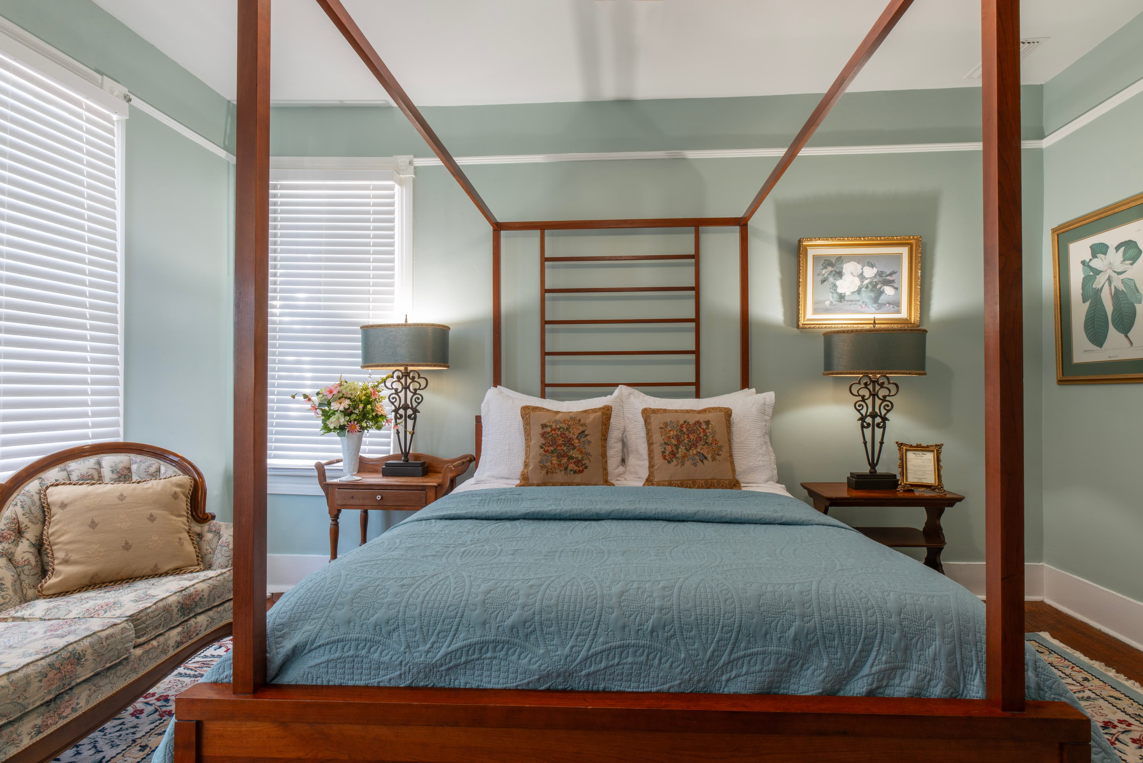 Bedroom in tranquil shades of blue with queen canopy bed, Victorian-style couch, and nightstands with table lamps flanking bed