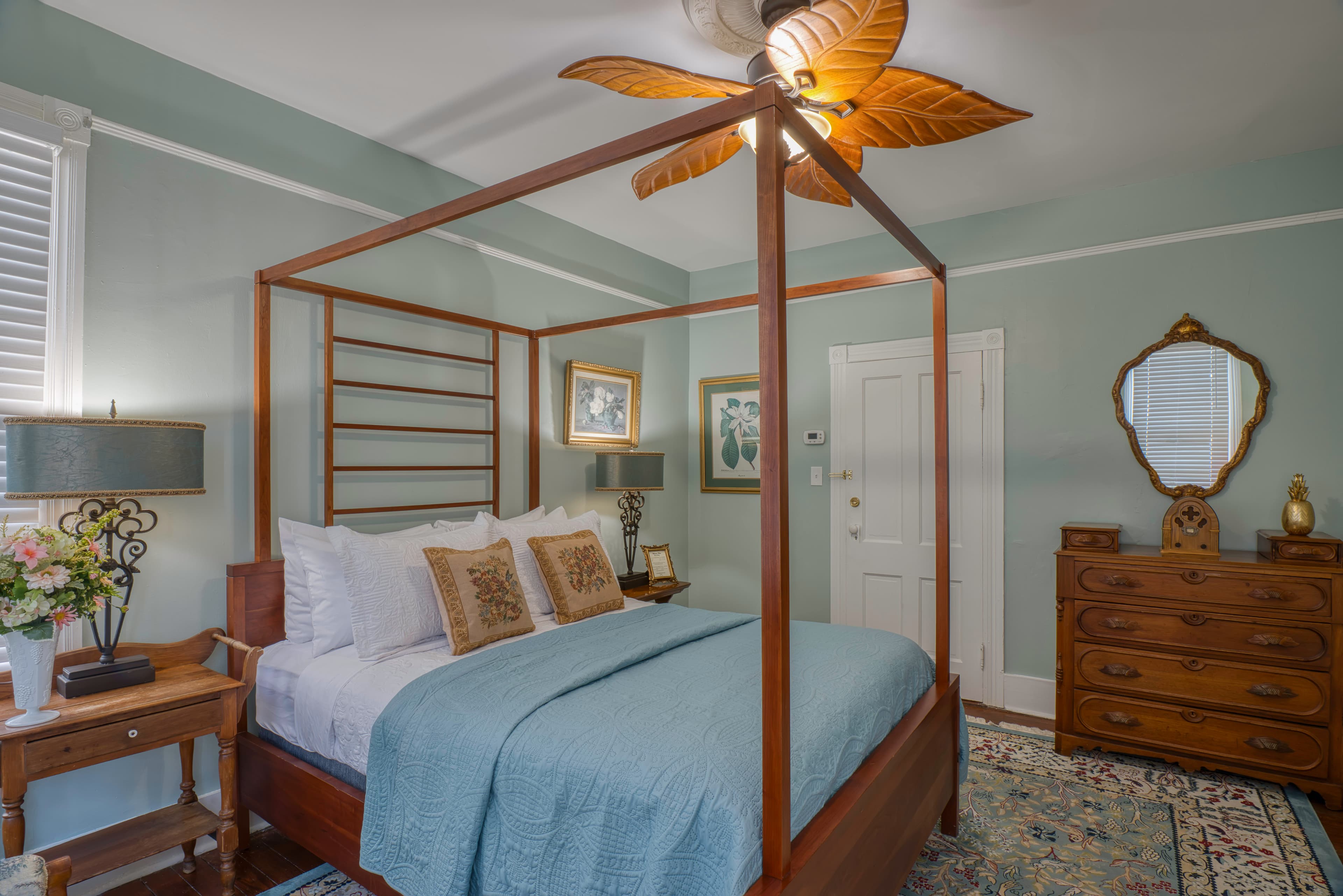 Bedroom with queen canopy bed, ceiling fan with leaf-shaped blades, wooden dresser,