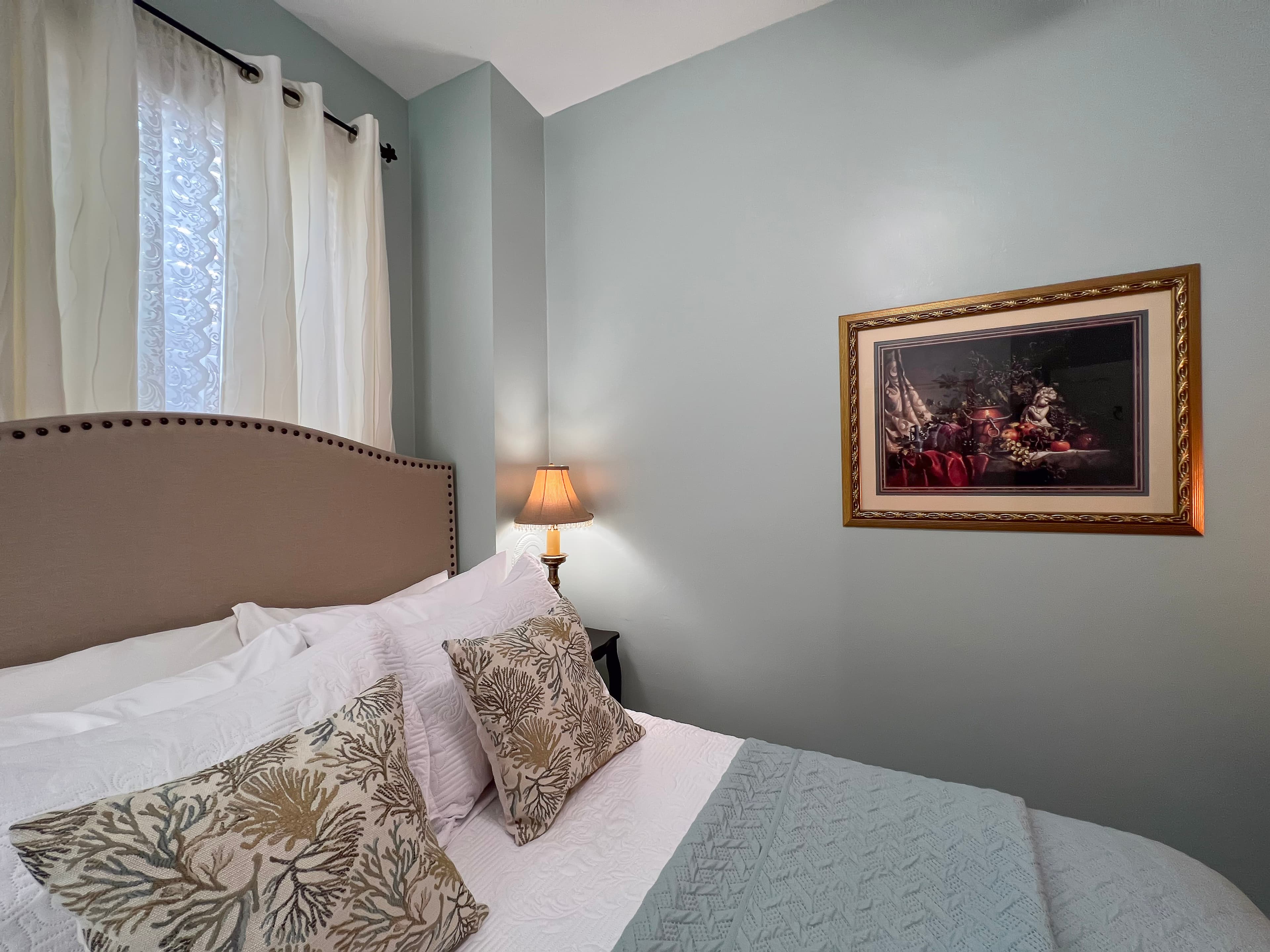 Inviting bedroom in shades of blue & white, double bed with upholstered headboard, nightstand with table lamp